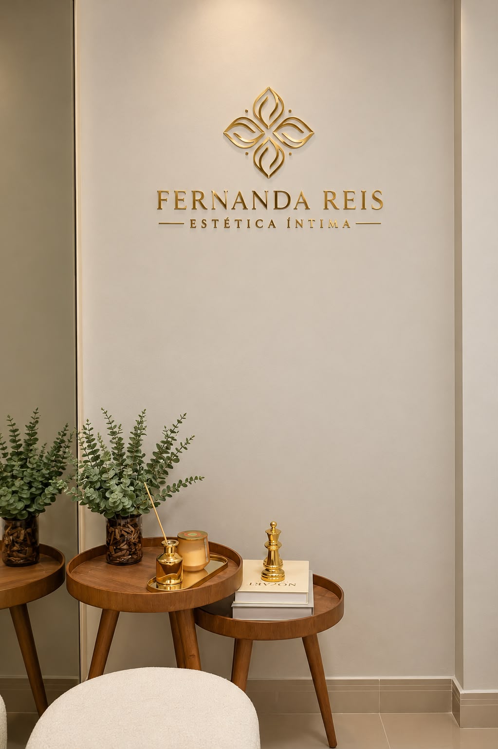 Espaço da clínica Fernanda Reis Estética Íntima, com logotipo dourado, plantas e mesas decorativas